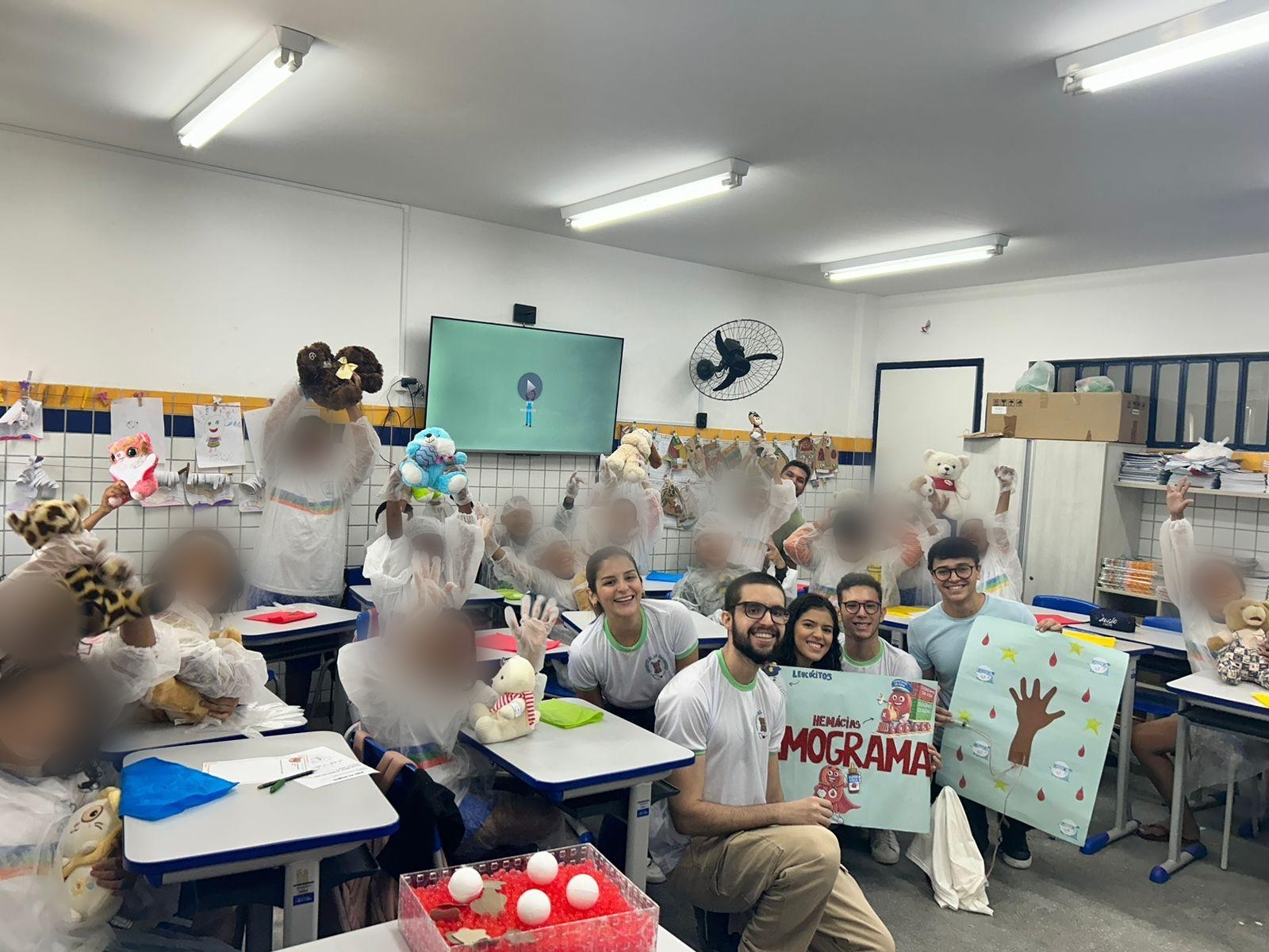 Turma reunida na sala de aula ao fim do evento, com crianças e integrantes levantando os ursinhos de pelúcia